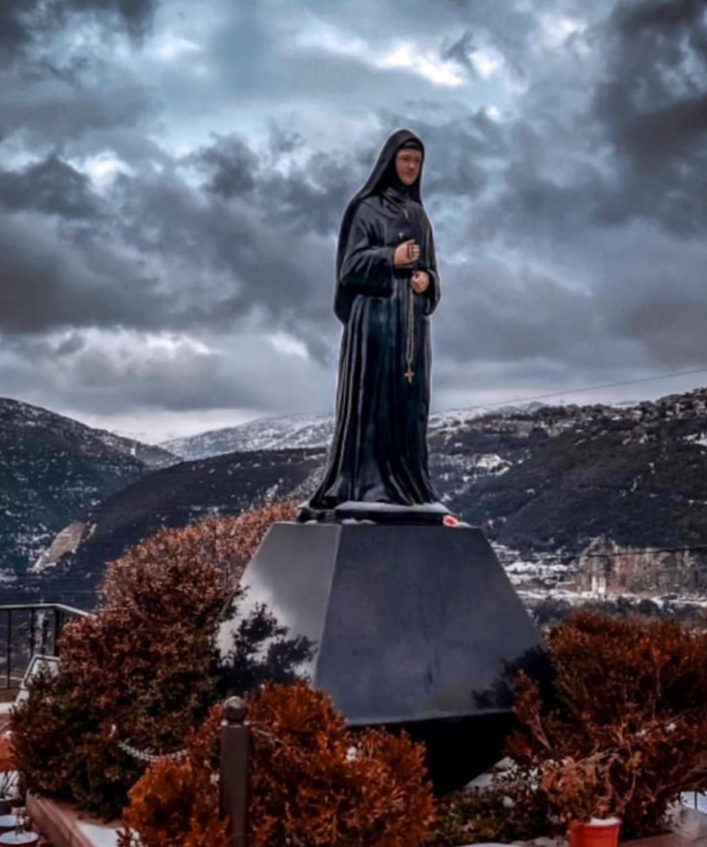 Estatua de bronce de santa Rafqa sobre su pedestal hexagonal, en un día de invierno sobre Hemlaya.